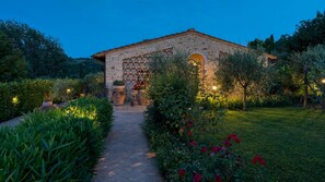 A stone building with a tiled pathway leading to it, surrounded by lush greenery and flowering plants. - Villa Sorripa 6, Emma Villas (Firenze)