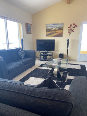 A living room with a sofa, a glass coffee table, a flat-screen TV, and a painting on the wall.