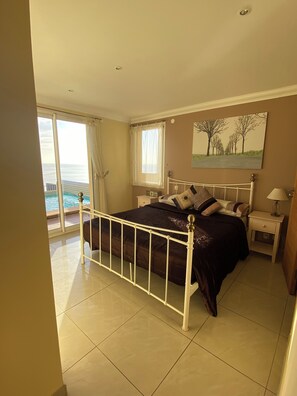 A bedroom with a bed, a nightstand, a lamp, a painting, a window with curtains, and a view of the sea. - Mediterranean villa with pool and magnificent sea views and walks (Cerbère)