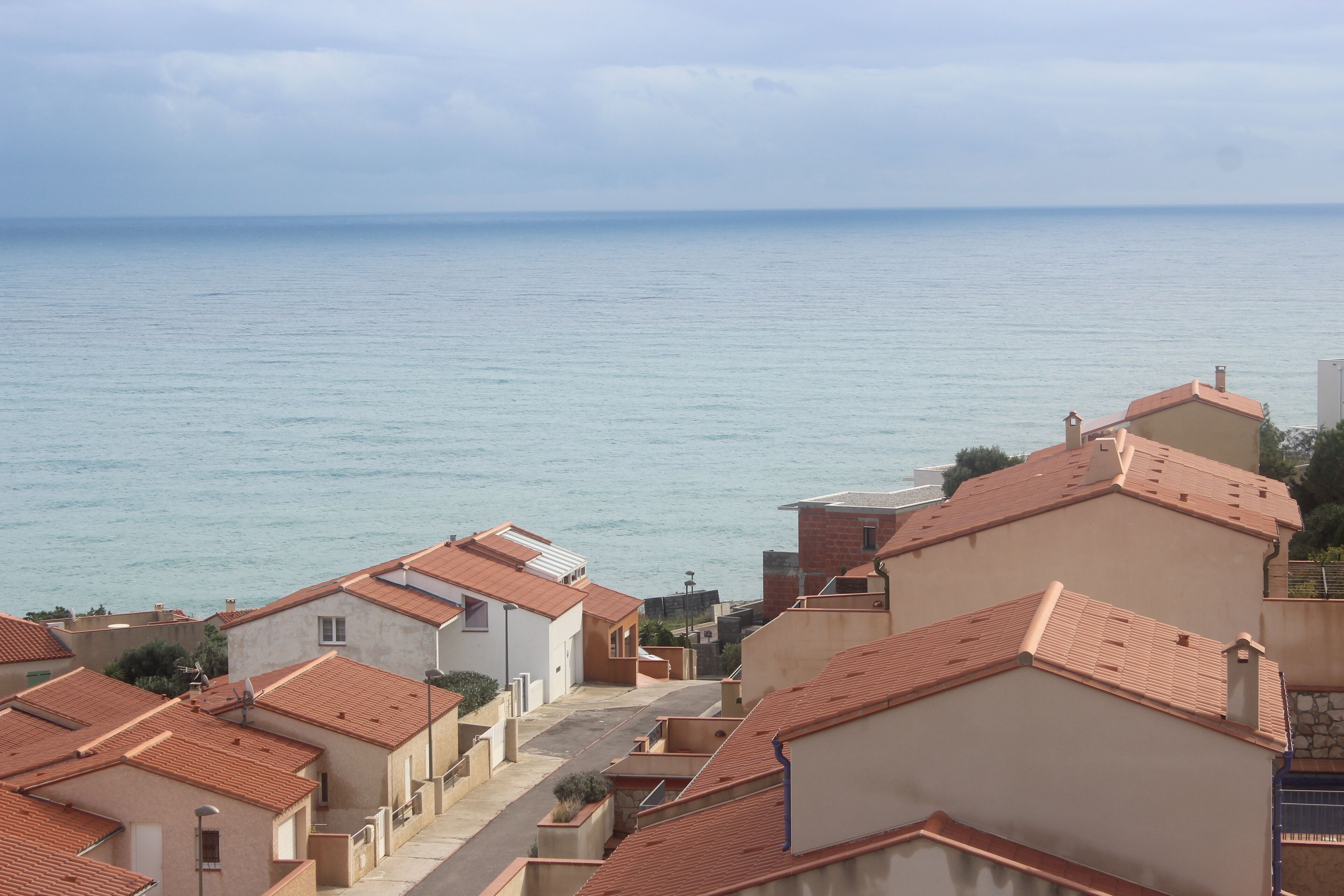 A coastal residential area with terracotta-roofed buildings and a view of the sea.