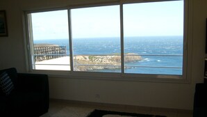Quarto com uma grande janela que oferece vista para o oceano e uma costa rochosa.