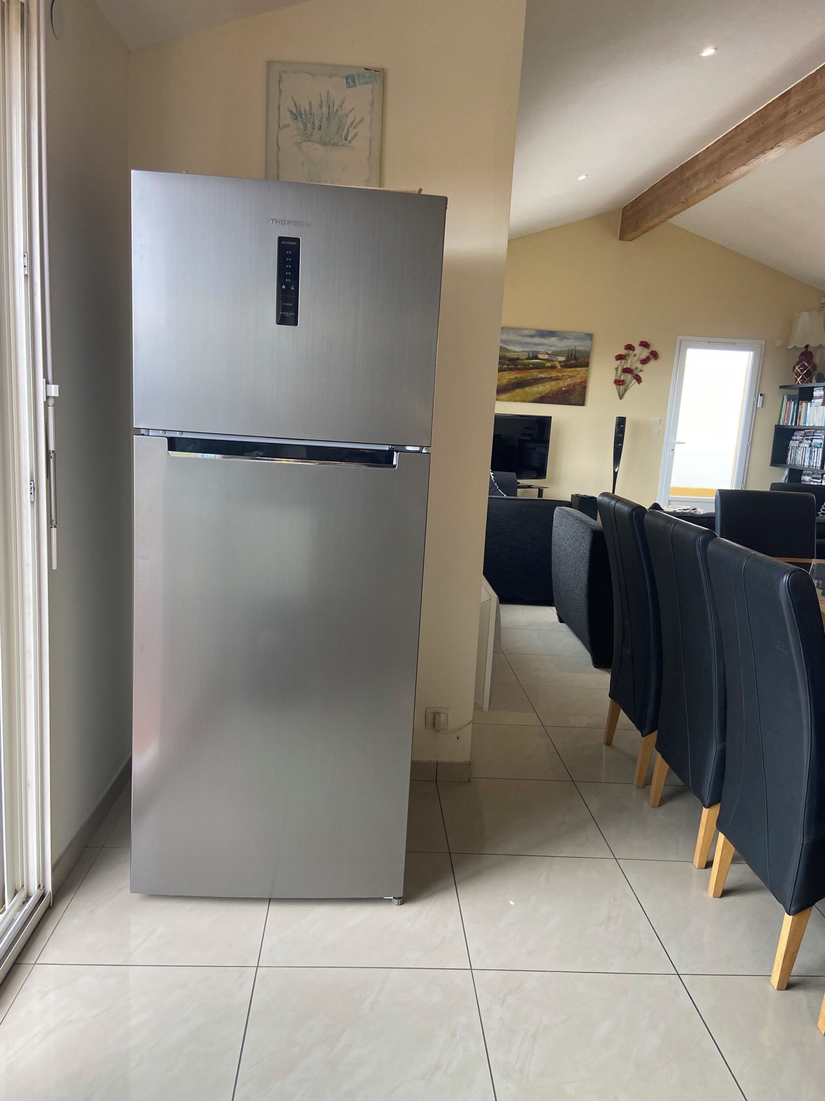 A modern kitchen with a stainless steel refrigerator, a dining area with dark chairs, and a painting on the wall.