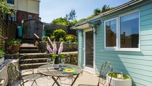 A patio with a table and chairs, a bottle of wine, and a book. - Homestead, Lyme Regis is a cosy riverside cabin, 10 mins walk from the beach (Lyme Regis)