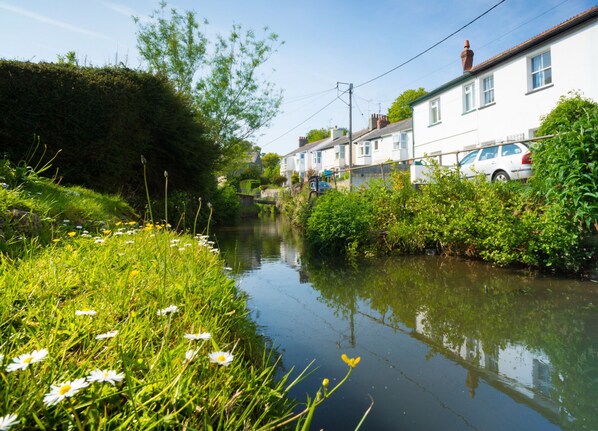 Un étroit canal bordé d’un côté par une rangée de maisons blanches et de l’autre par une zone herbeuse parsemée de marguerites.