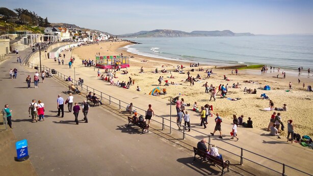 A beach with a promenade, benches, and people walking. - Homestead, Lyme Regis is a cosy riverside cabin, 10 mins walk from the beach (Lyme Regis)