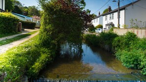 A narrow water channel with a small waterfall, surrounded by lush greenery and residential buildings. - Homestead, Lyme Regis is a cosy riverside cabin, 10 mins walk from the beach (Lyme Regis)