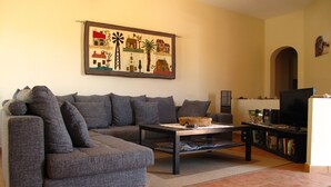 Ein Wohnzimmer mit grauem Sofa, einem Couchtisch, einem Fernseher und einem Bücherregal.