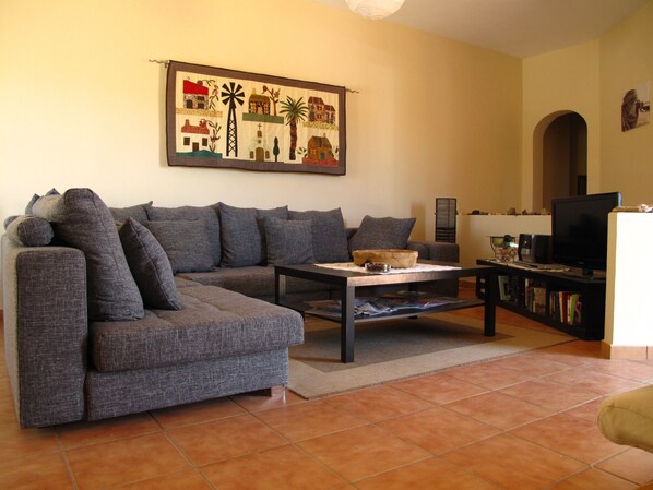 Una sala de estar con un sofá gris, una mesa de centro, un televisor y una estantería.
