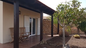 Ein überdachter Patio-Bereich mit einer Steinwand, einem Holzstuhl und einem kleinen Baum.