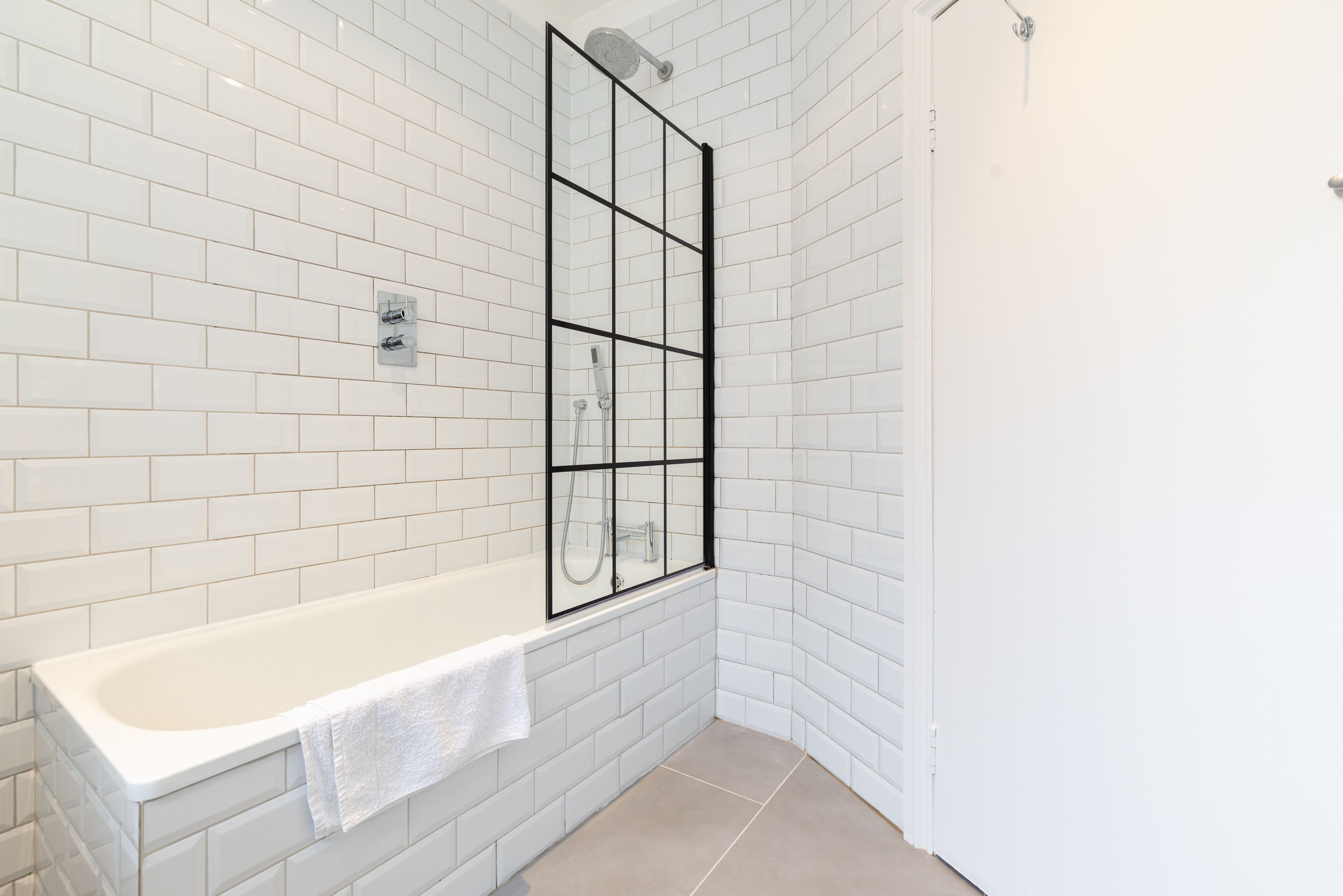 Un baño con paredes de azulejos blancos, una bañera blanca y una cabina de ducha de vidrio.