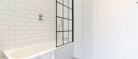 Un baño con paredes de azulejos blancos, una bañera blanca y una cabina de ducha de vidrio.