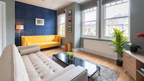 Ein modernes Wohnzimmer mit einem weißen Sofa, einem gelben Sofa, einem schwarzen Couchtisch und einem großen Fenster mit Blick auf Gebäude.
