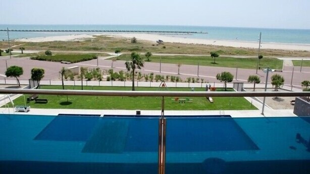 Blick vom Balkon auf einen Strand mit einem Schwimmbecken im Vordergrund.