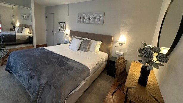 Un dormitorio con una cama grande, mesitas de noche, un espejo y un pequeño escritorio con un florero.
