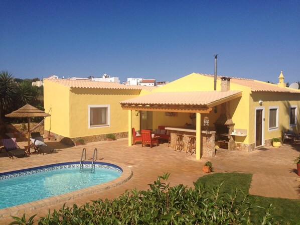 A yellow villa with a swimming pool, outdoor seating, and a barbecue area.