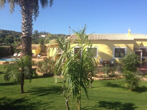 A yellow villa with a tiled roof, surrounded by a well-maintained lawn and palm trees.