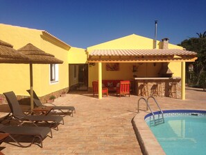 A pool area with lounge chairs, a barbecue, and a covered patio.