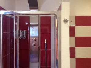 A modern bathroom with a glass shower enclosure, red and white tiled walls, and a visible towel rack.