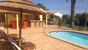 Un área de piscina con sillas de descanso y una estructura con techo de paja.