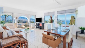 A modern living room with a large TV, comfortable seating, and a dining area with a view of the ocean. - Private Garden & pool, Sea View, near restaurant, free Wi-fi, 5,5 km from Beach (La Matanza de Acentejo)