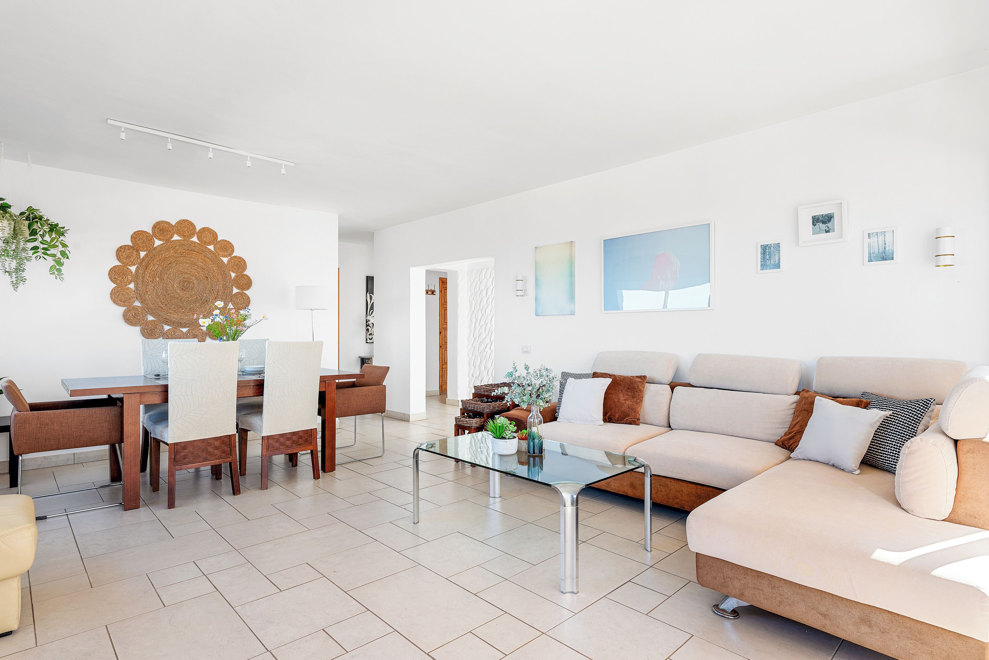A modern living room with a glass coffee table, a beige sofa, and a dining area with wooden chairs and a white table.