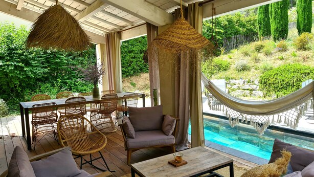 A covered outdoor seating area with wicker furniture, a hammock, and a view of a swimming pool. - Local stone Provencal country cottage with pool  (Saint-André-De-Roquepertuis)