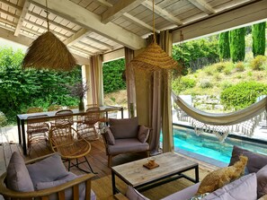 A covered outdoor seating area with wicker furniture, a hammock, and a view of a swimming pool. - Local stone Provencal country cottage with pool  (Saint-André-De-Roquepertuis)