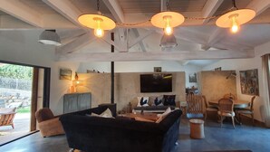 A spacious living room with a black sofa, wooden dining table, and a fireplace. - Local stone Provencal country cottage with pool  (Saint-André-De-Roquepertuis)