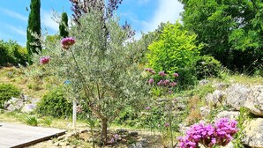 A garden with a variety of plants and flowers, including purple blooms, a wooden deck, and a stone pathway. - Local stone Provencal country cottage with pool  (Saint-André-De-Roquepertuis)