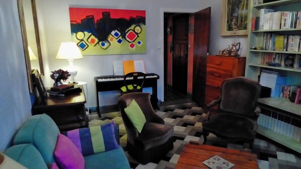 A living room with a checkered floor, a piano, a bookshelf, and a painting on the wall.