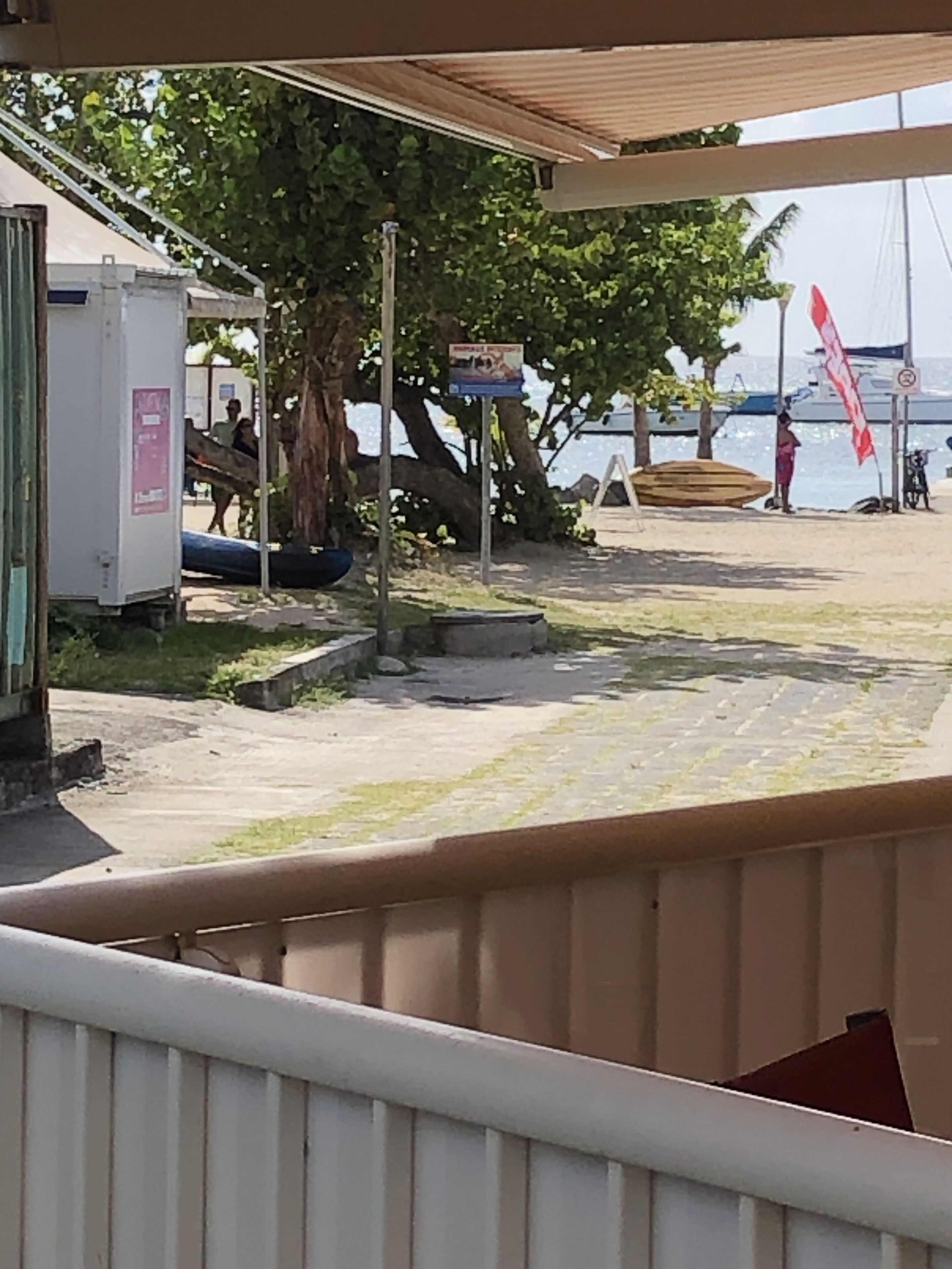 Ett område vid stranden med ett takförsett sittområde, en båt och en skylt.