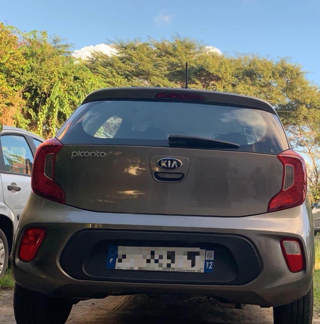 Ein Kia Picanto parkt draußen, das Heck ist sichtbar und weist ein Nummernschild auf.