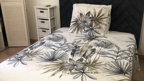 En säng med ett blommigt överkast och en kudde, ett sängbord med lådor och en garderob med horisontella ribbor.