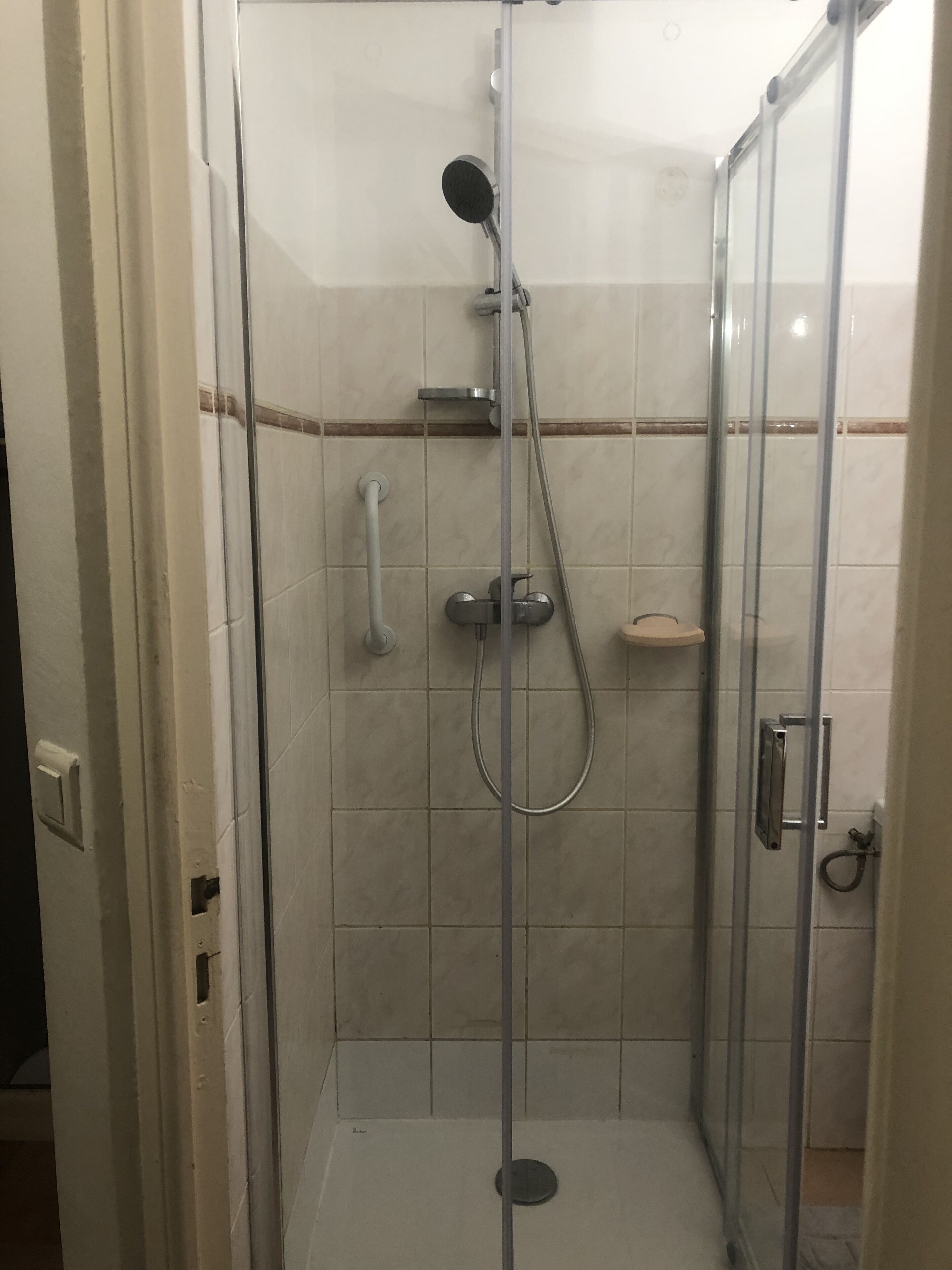 Une cabine de douche fermée par des parois en verre, dotée d’un pommeau de douche à main, d’un robinet mural et d’un autre pommeau de douche à main.
