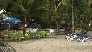 Ett sandstrandområde med rader av gröna och vita solstolar, varav några står i skuggan under parasoller.