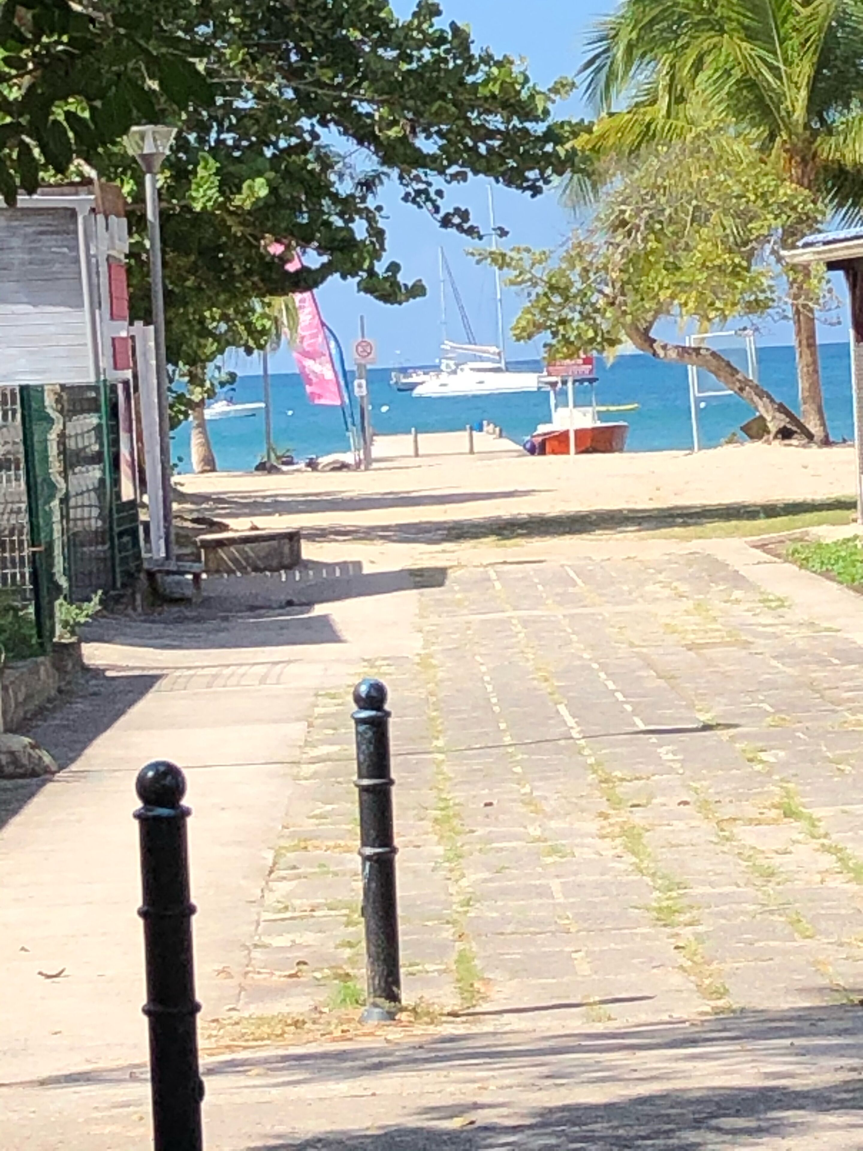Ein gepflasterter Weg führt zu einer Uferpromenade, im Hintergrund liegt ein Boot angedockt.