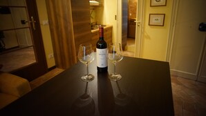 A bottle of wine and two glasses on a table in a room with wooden flooring and a door leading to another room.