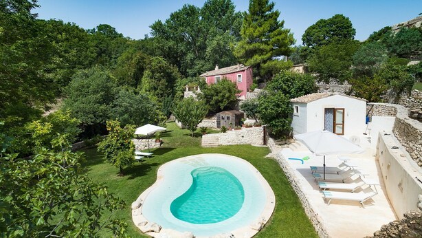 Ein privater Pool, umgeben von einem gepflegten Rasen, mit einer Steinsichtmauer und einem kleinen Gebäude im Hintergrund.