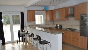 Una cocina moderna con armarios de madera, una isla grande con taburetes de bar, horno empotrado y puerta corrediza de vidrio que da a un patio.