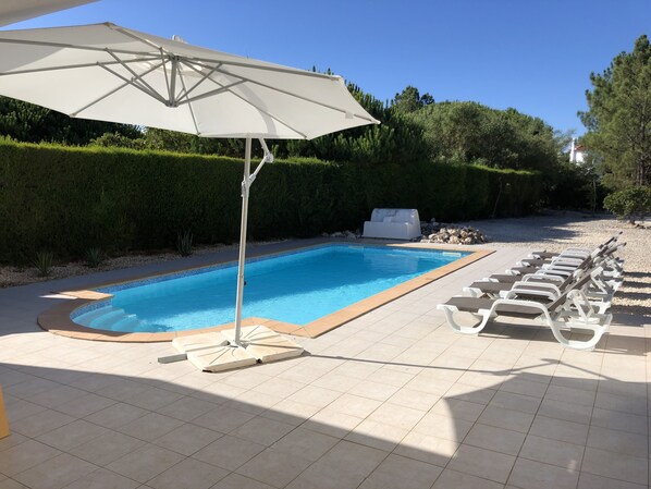 A swimming pool with lounge chairs and a white umbrella.