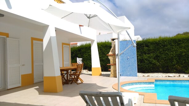 Un espacio al aire libre cubierto con piscina, una mesa y sillas, y una estructura de piedra.