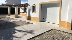 Un edificio blanco con patio empedrado, puerta de garaje y pérgola con hamaca.