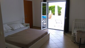 Un dormitorio con cama, mesita de noche, puerta y vistas a un espacio exterior con piscina y sillas.