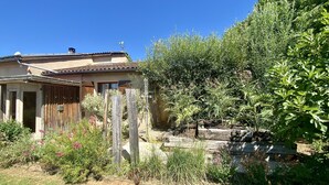 Una casa con techo de tejas, valla de madera y jardín con diversas plantas y flores.