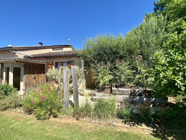 Una casa con techo de tejas, valla de madera y jardín con diversas plantas y flores.