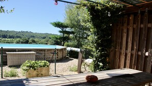 Una terraza de madera con una mesa, una planta en maceta y una vista de una piscina e árboles al fondo.