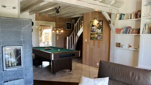 Un salón acogedor con mesa de billar, chimenea, escalera y estantería.