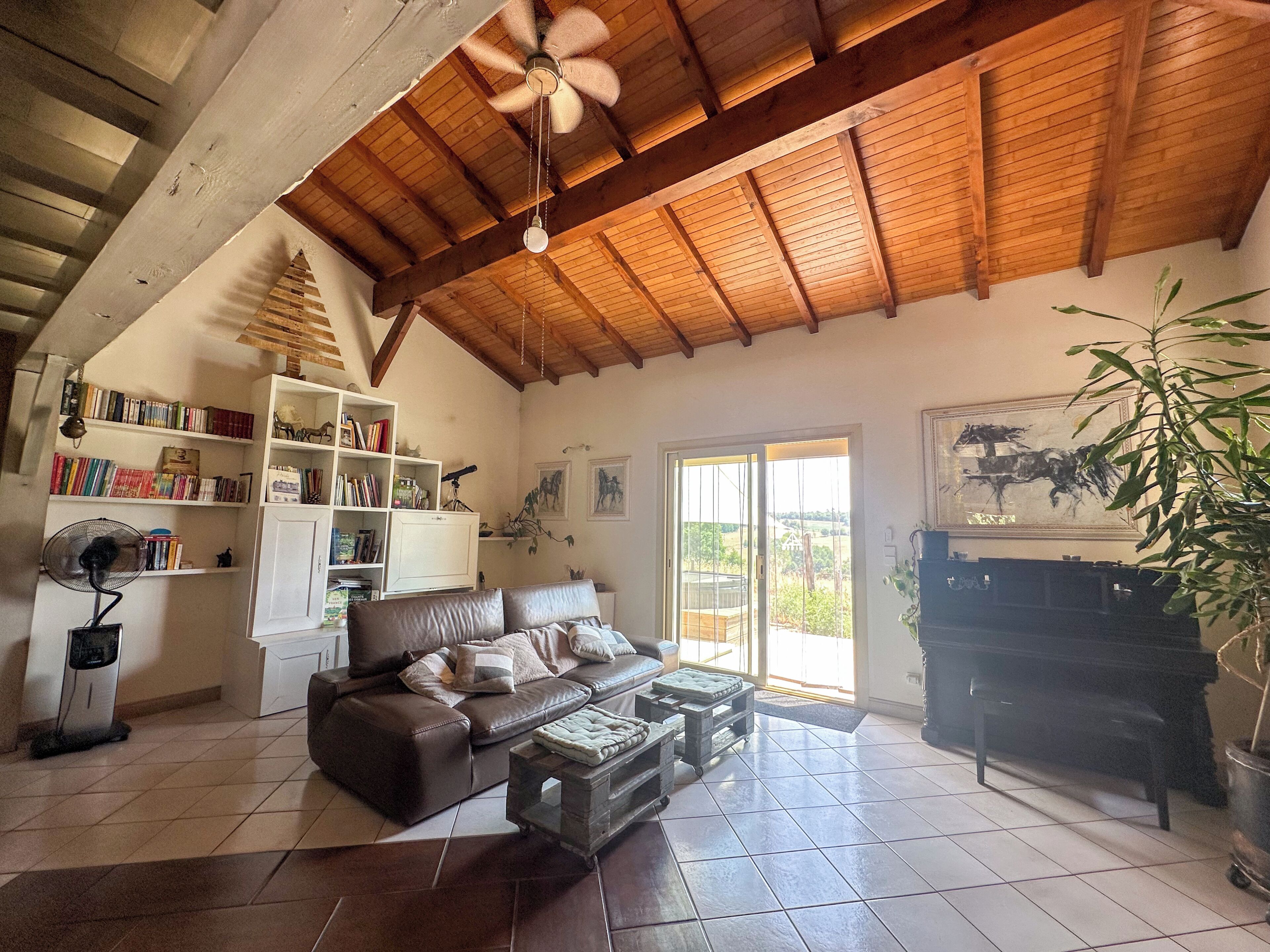 A spacious living room with a high ceiling, a leather sofa, a bookshelf, and a piano.