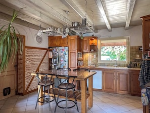 Une cuisine avec des meubles de rangement en bois, un réfrigérateur en acier inoxydable, une table à manger en bois avec des chaises, et un luminaire suspendu.