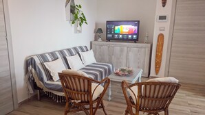 Een woonkamer met een gestreept bankje, twee rieten stoelen, een televisie, een klein kastje en een decoratieve plant.